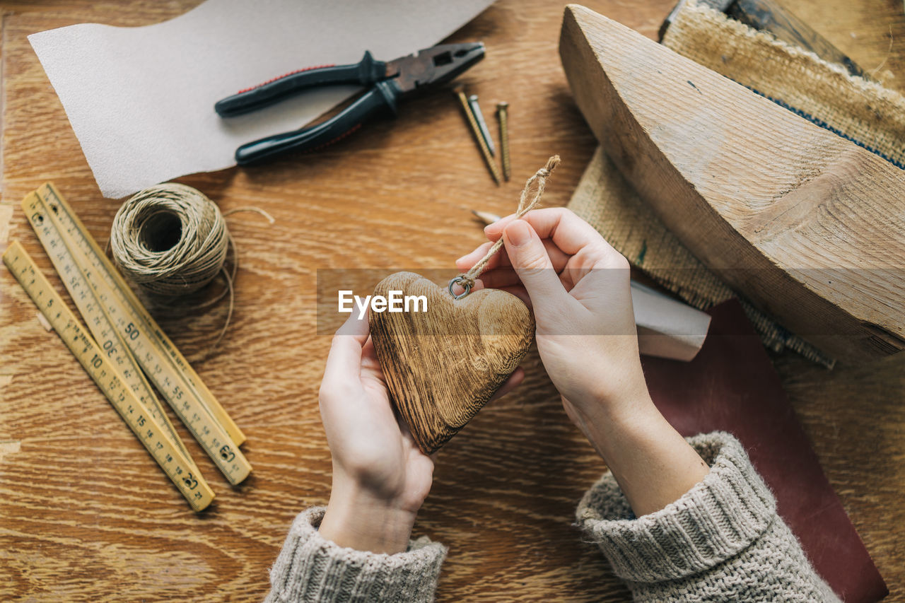 Cropped hands of woman holding wooden heart shape at table