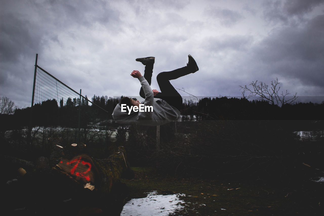 Young man jumping in mid air against cloudy sky