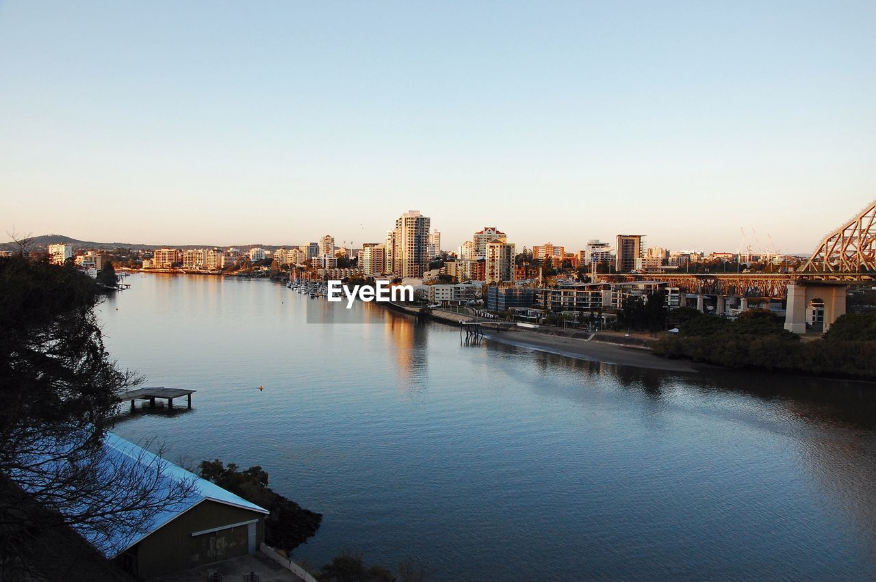 Buildings by river against clear sky in city