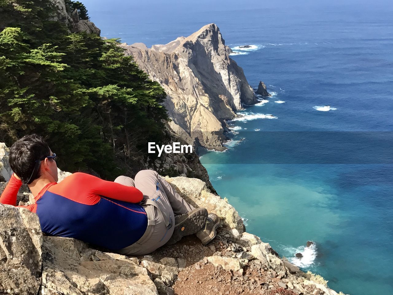 High angle view of man sitting on cliff against sea