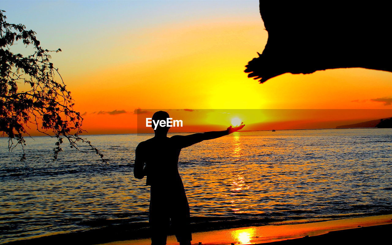 SILHOUETTE MAN STANDING ON BEACH DURING SUNSET