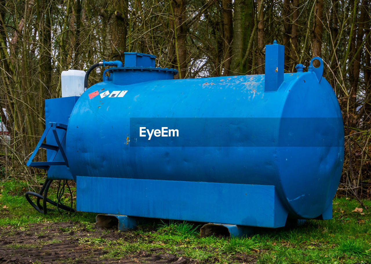 BLUE CONTAINER ON FIELD AGAINST TREES AND PLANTS