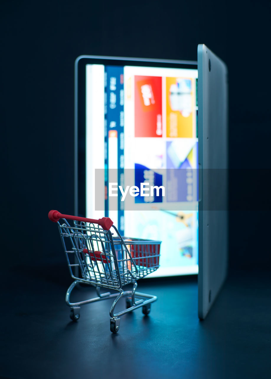 Close-up of shopping cart by digital tablet against black background