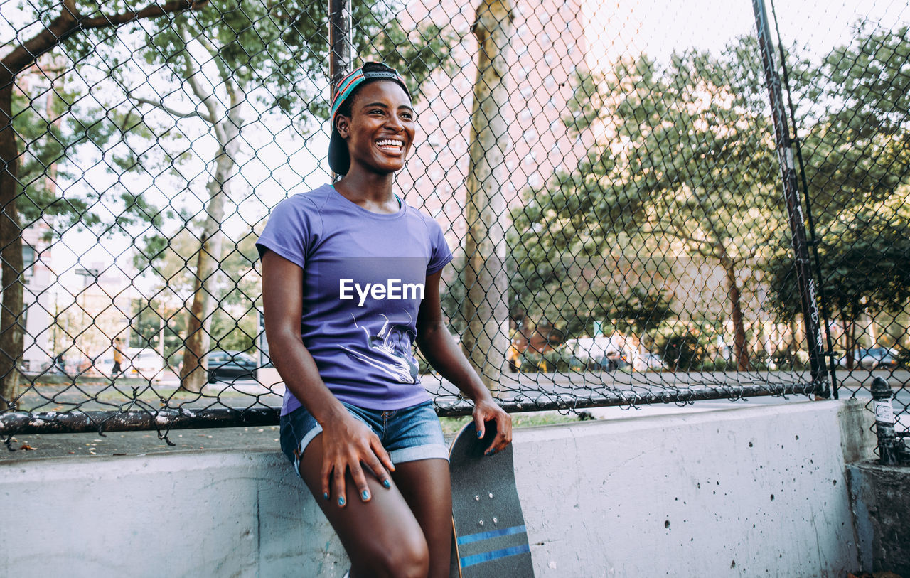 PORTRAIT OF SMILING YOUNG WOMAN STANDING OUTDOORS