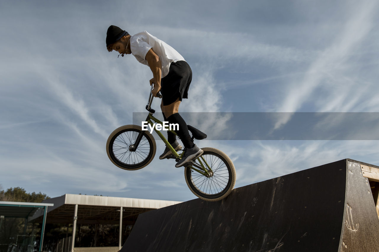 Young man jumping on ramp at bike park against sky