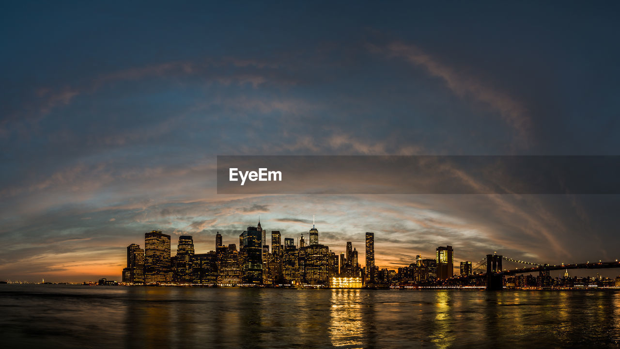 Illuminated city at waterfront during sunset