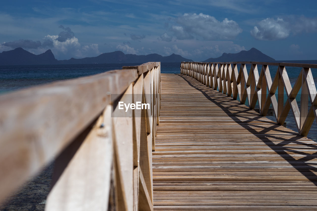 Wooden bridge pier over sea against sky