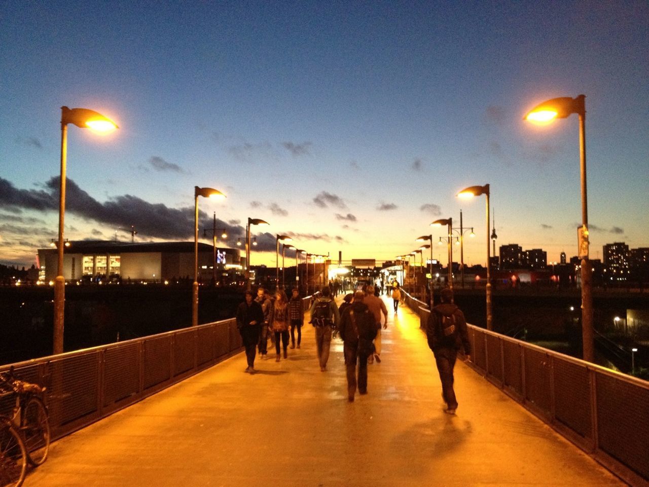 People walking on illuminated bridge at dusk