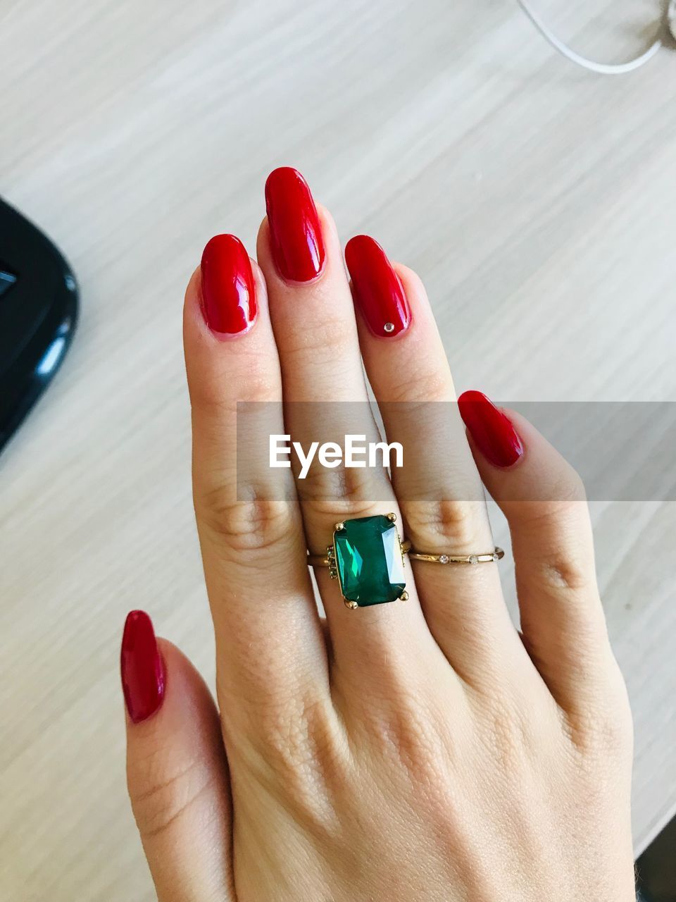 Cropped hand of woman wearing emerald ring with red nail polish on table