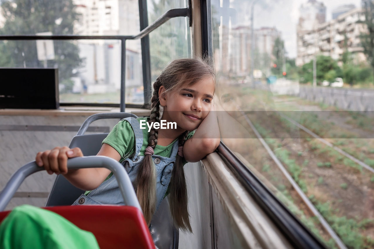 Young girl rides in empty tram and looks at the window dreamily, public transportation, city tramway