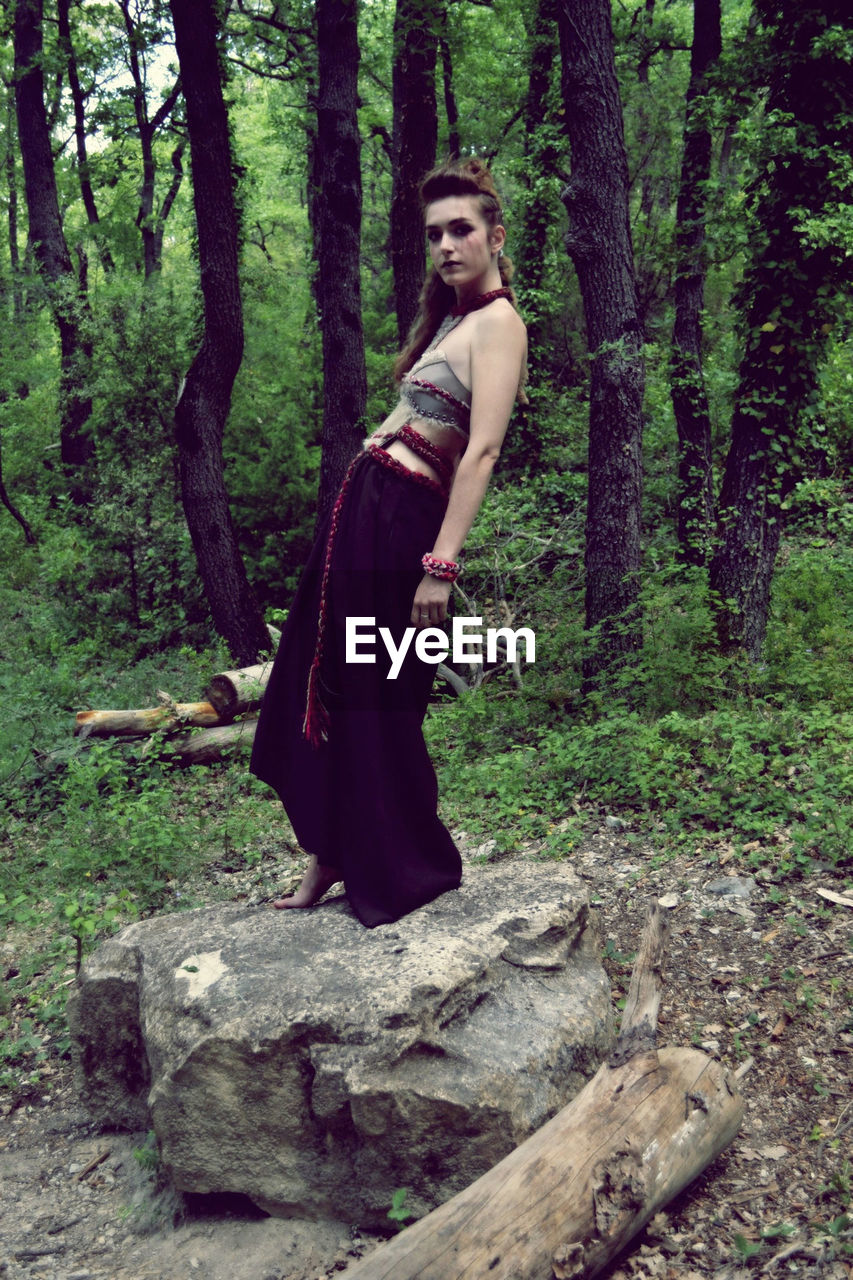 FULL LENGTH OF YOUNG MAN STANDING ON TREE TRUNK IN FOREST