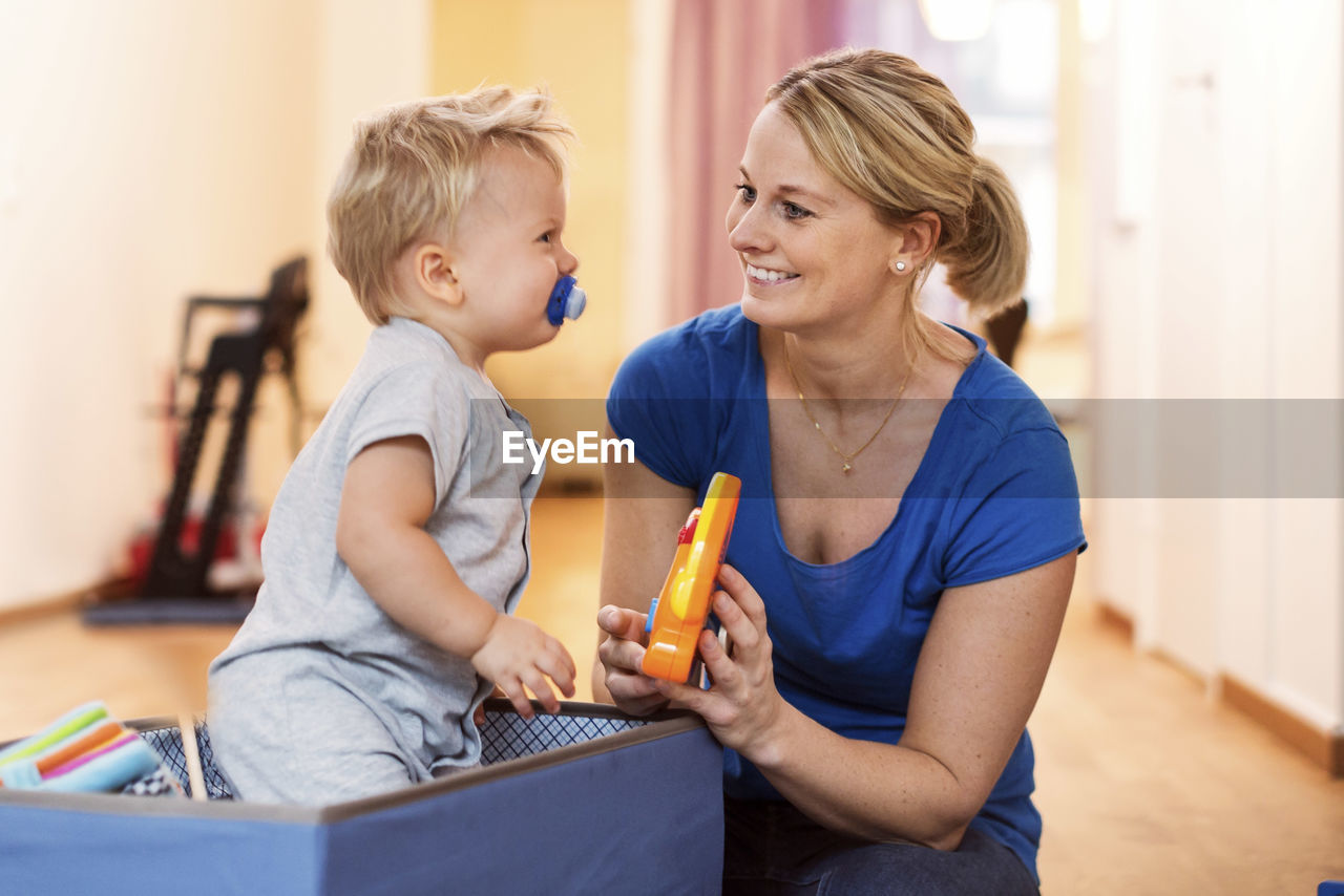 Happy woman playing toys with baby boy at home