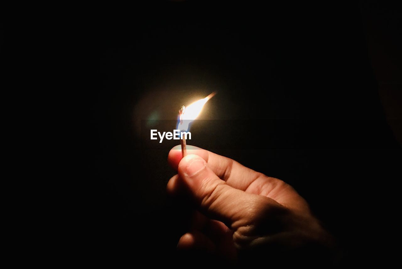 Close-up of hand holding burning matchstick in darkroom