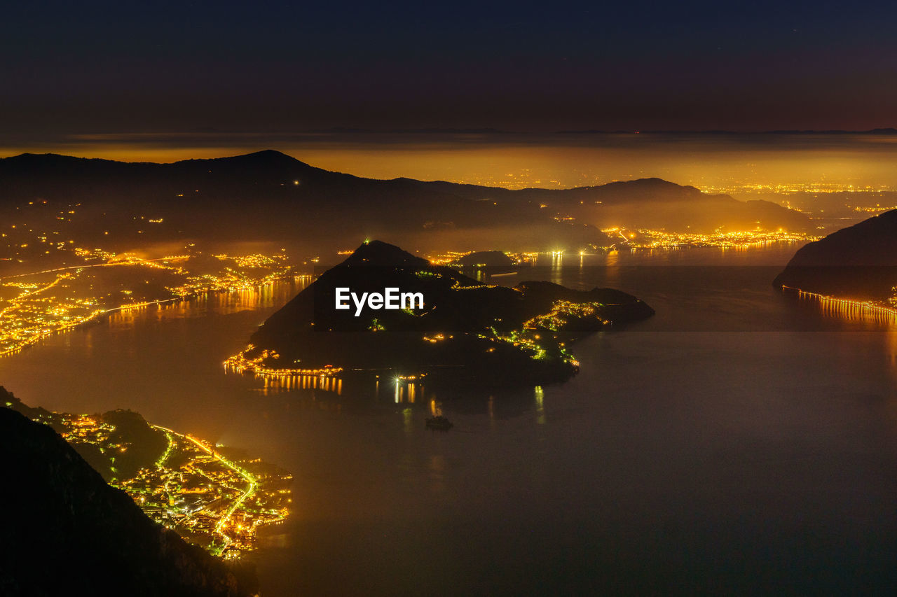 Aerial view of illuminated city by lake iseo against sky at night