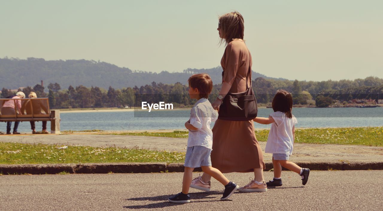 REAR VIEW OF MOTHER AND DAUGHTER STANDING ON SHORE AGAINST CLEAR SKY