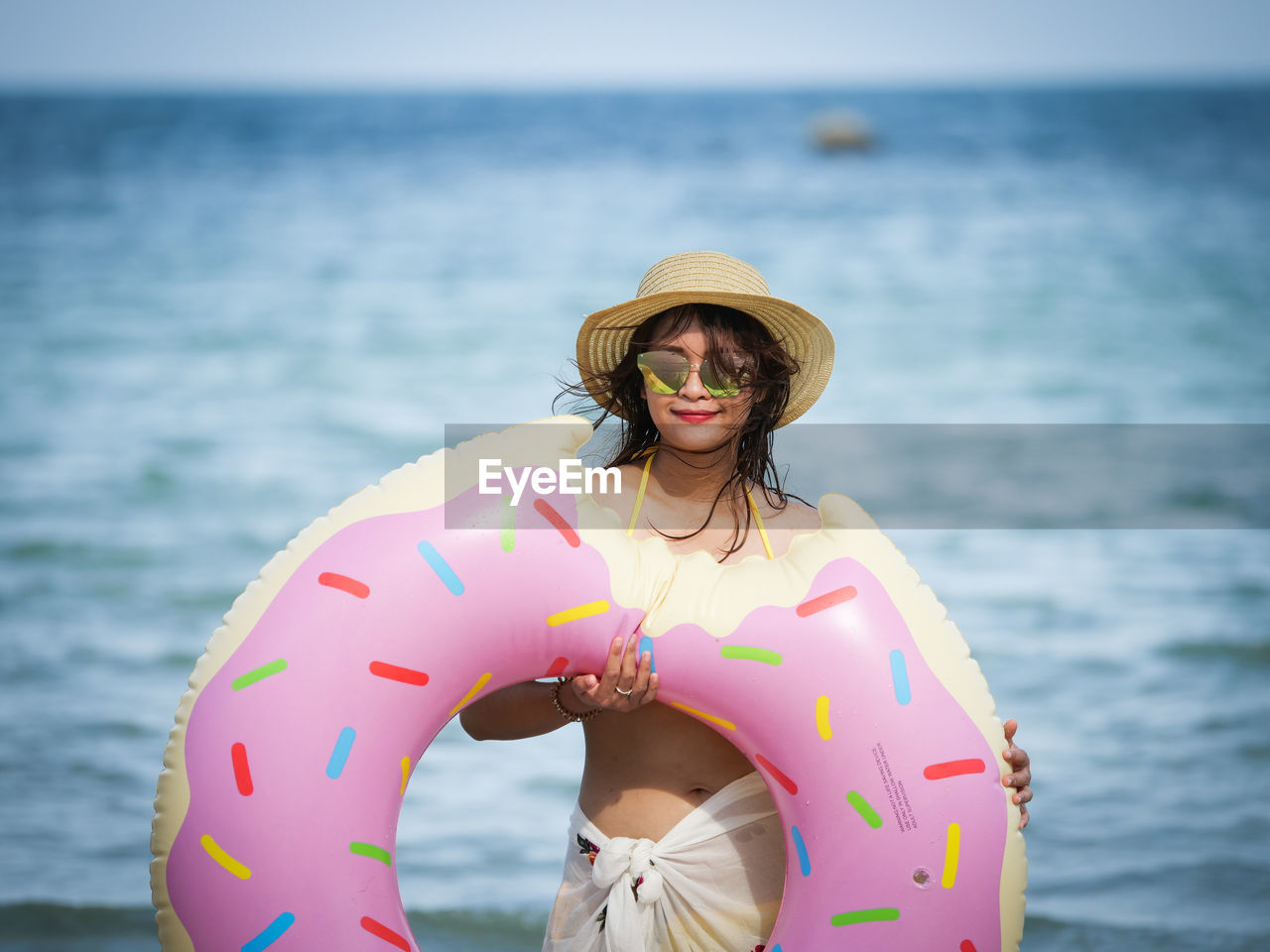 Portrait of woman holding donut pattern inflatable ring at beach