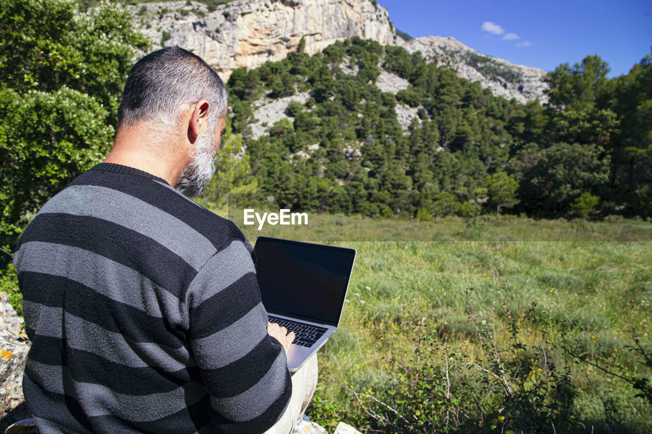 Traveler working remotely on netbook computer while enjoying of natural landscape outdoor