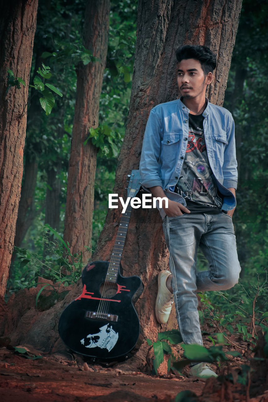 Full length of man standing with guitar by tree in forest