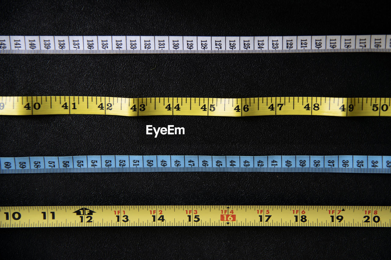 Various measuring tape in white, yellow and blue on black surface, overhead.