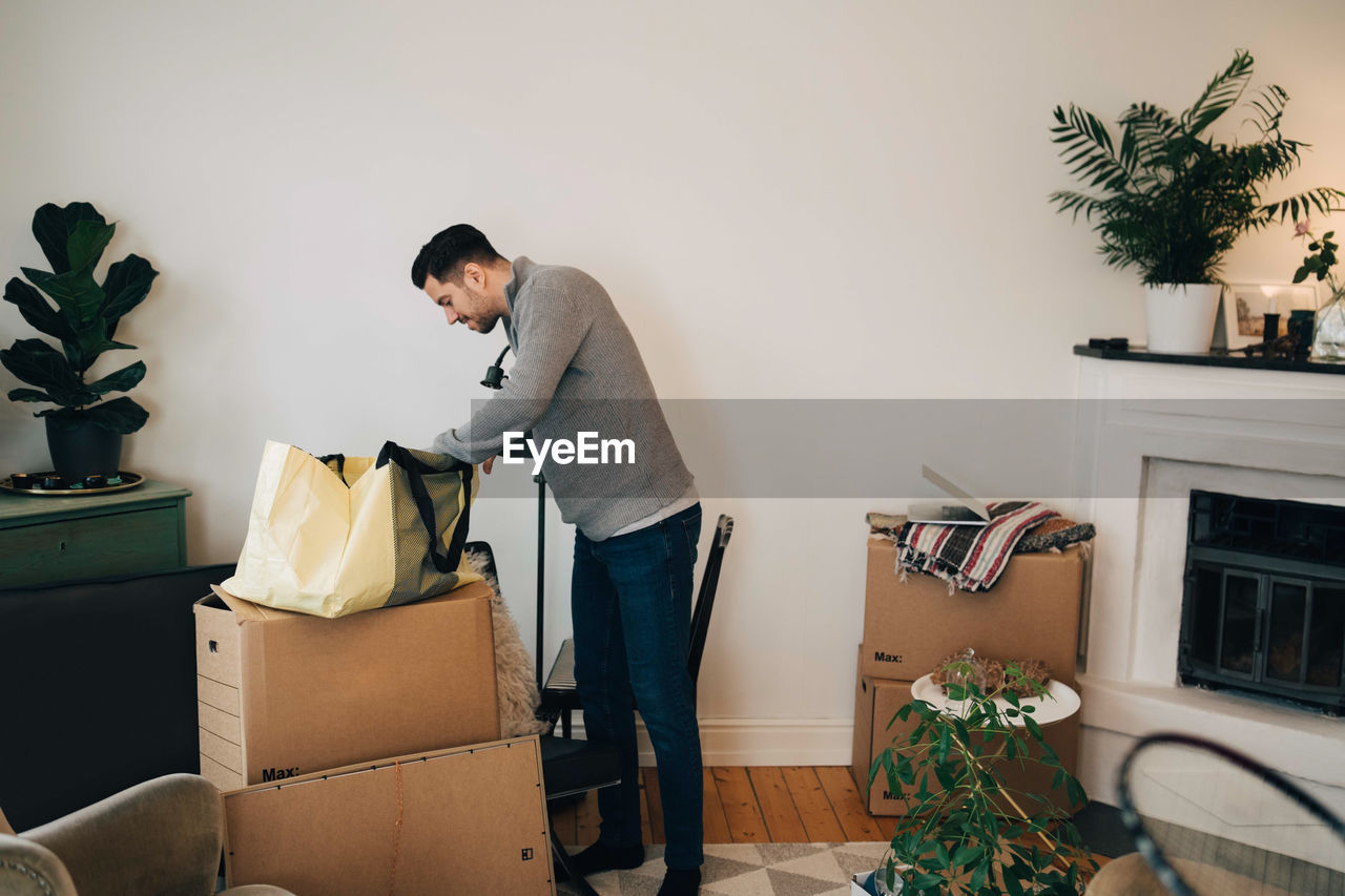 Man searching in bag while standing by wall at living room