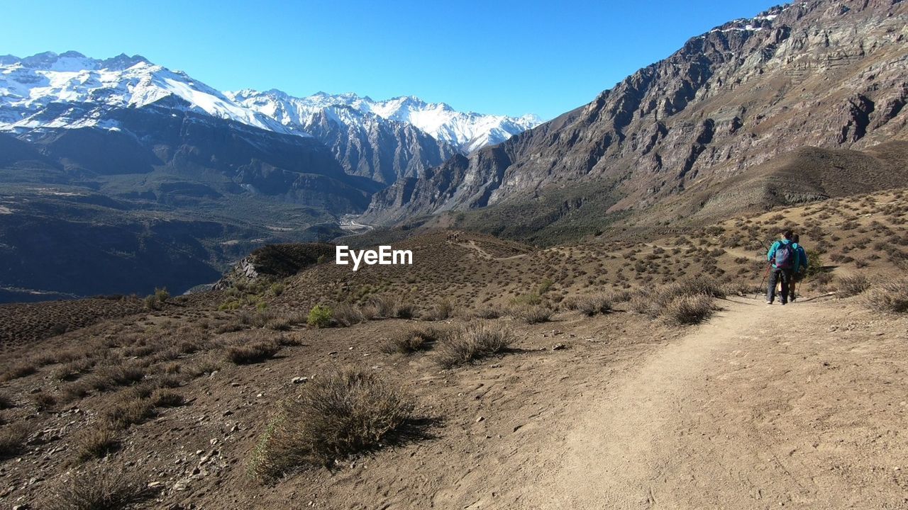 REAR VIEW OF MAN RIDING MOTORCYCLE ON SNOWCAPPED MOUNTAINS