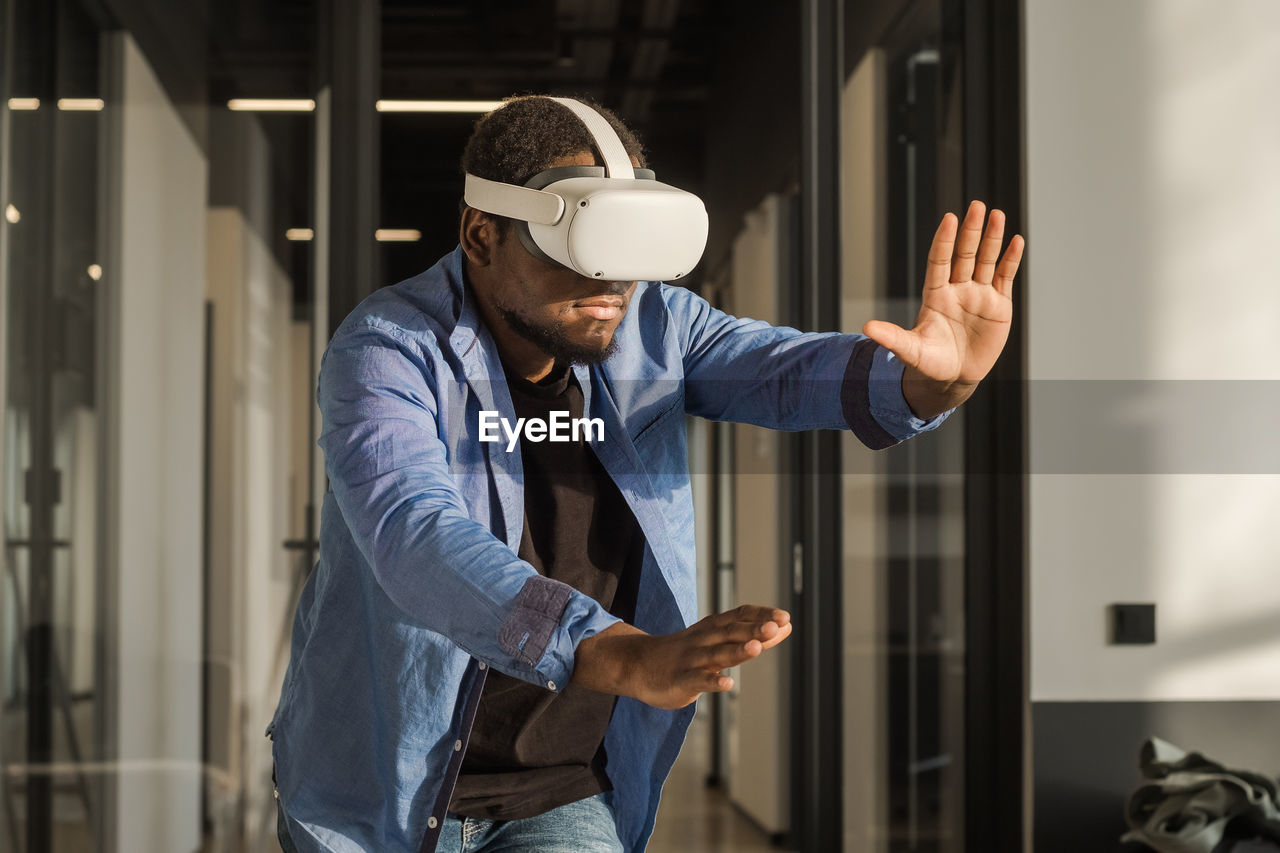Black man in vr headset exploring metaverse world, touching virtual reality subjects. cyber world