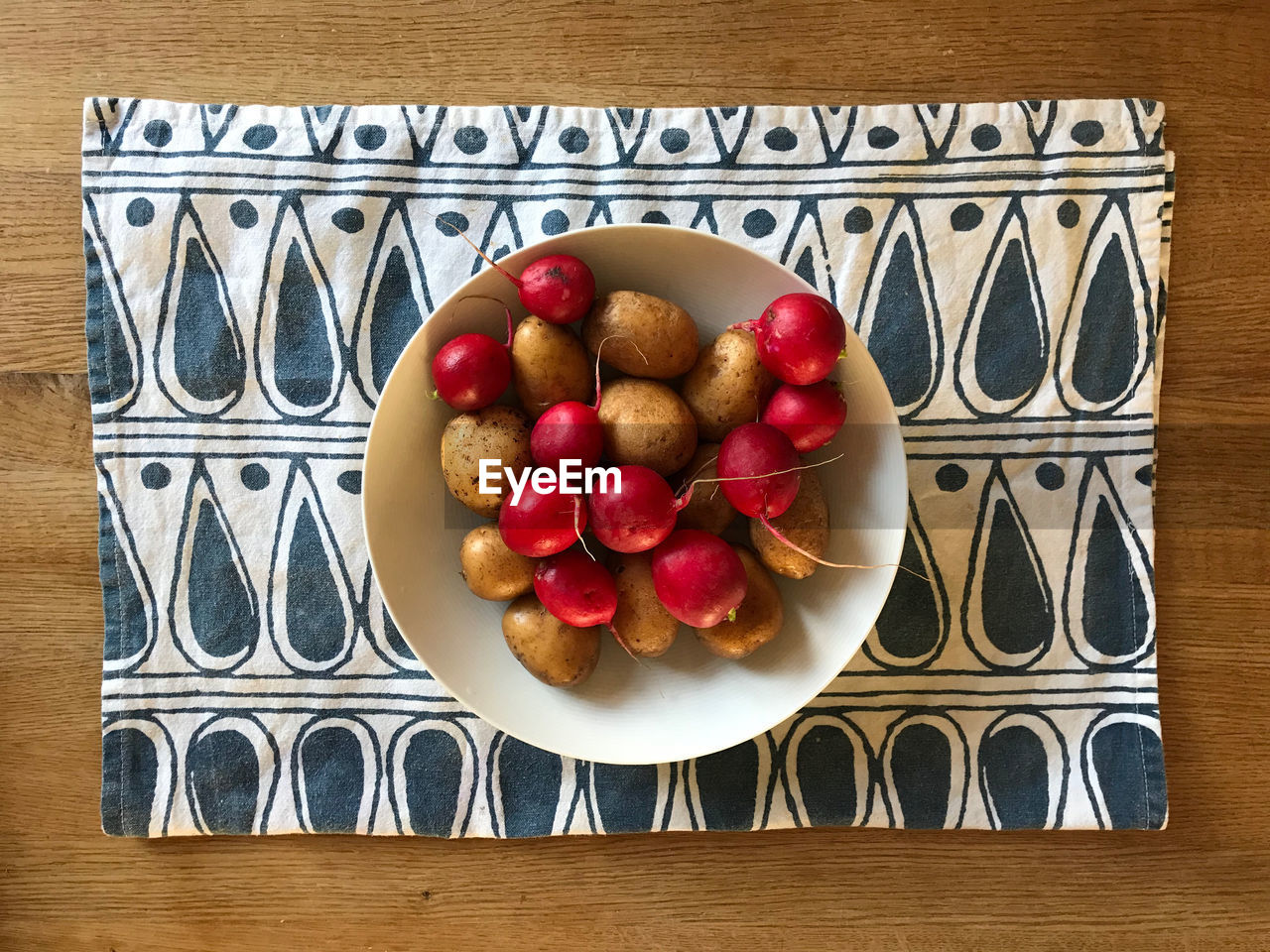 Directly above shot of potatoes and radishes on a tablecloth on a wooden kitchen table
