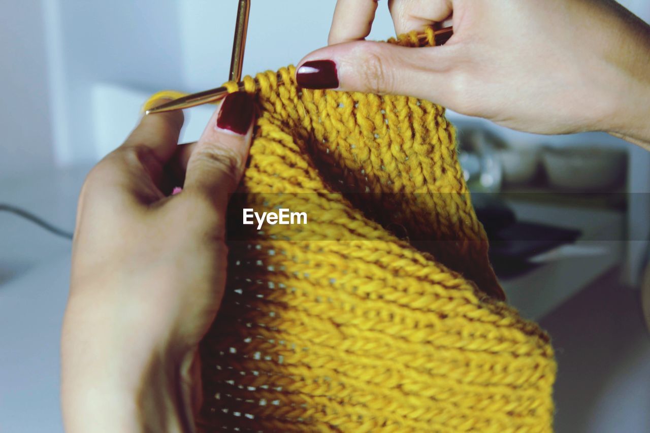 Cropped hands of woman knitting yellow fabric