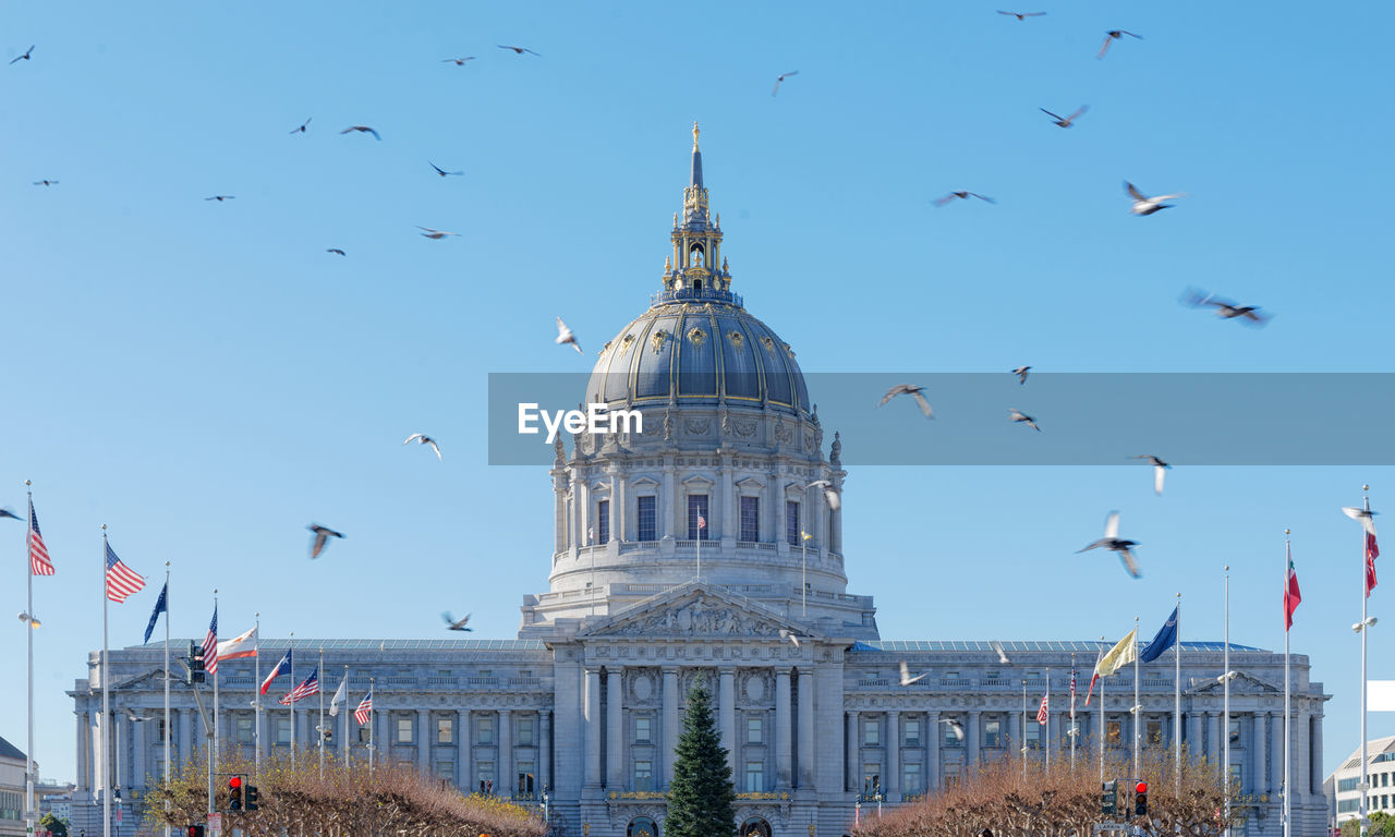 Flock of birds flying over church against sky