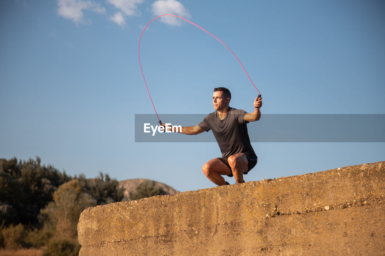 Low angle view of young man jumping against clear sky