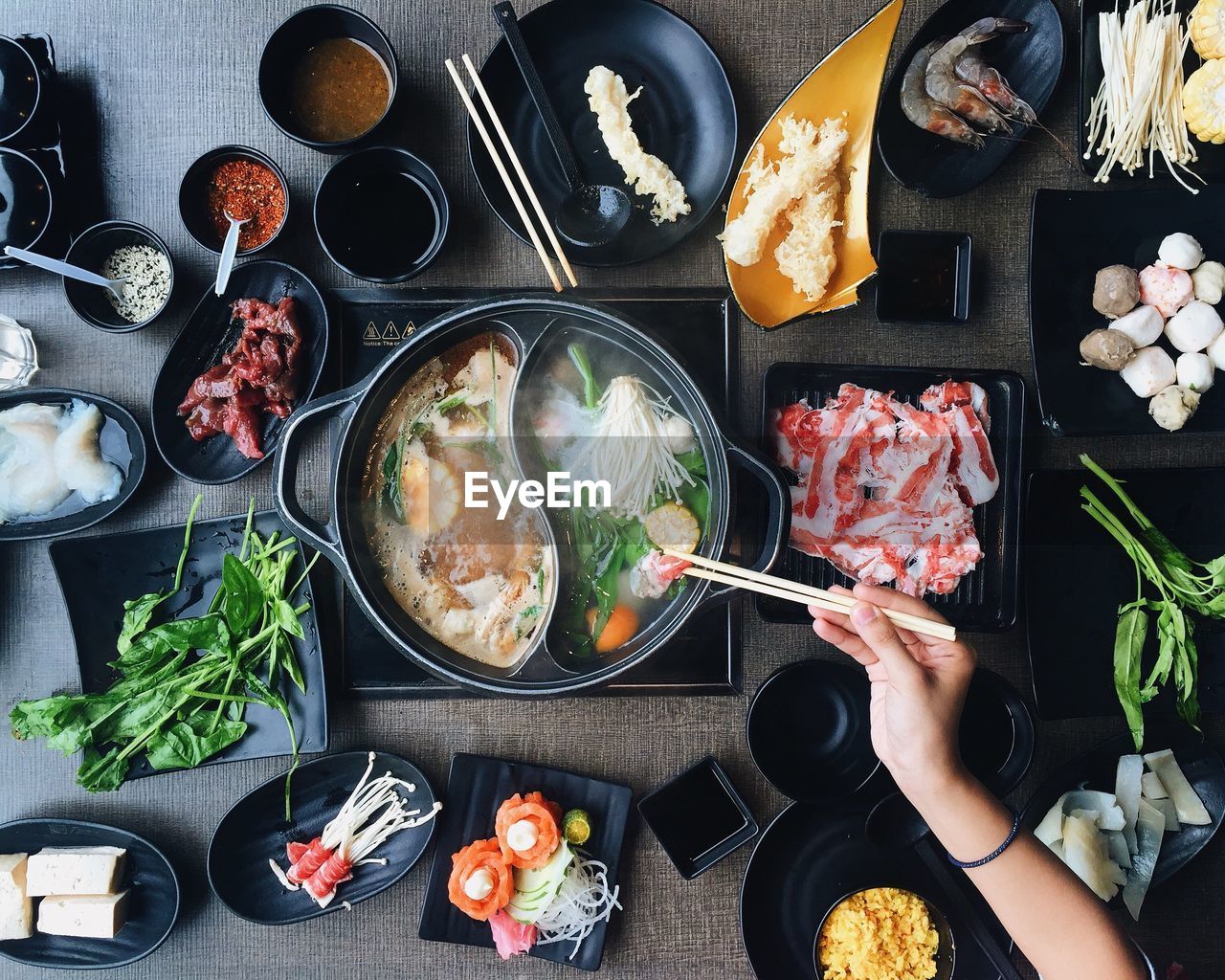 Cropped image of woman picking food from hot pot on table