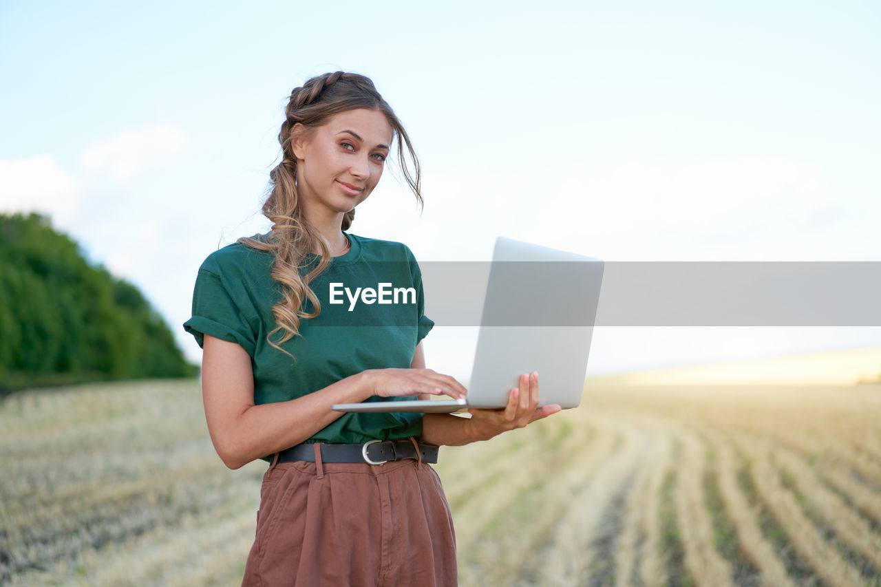 YOUNG WOMAN USING MOBILE PHONE ON FIELD