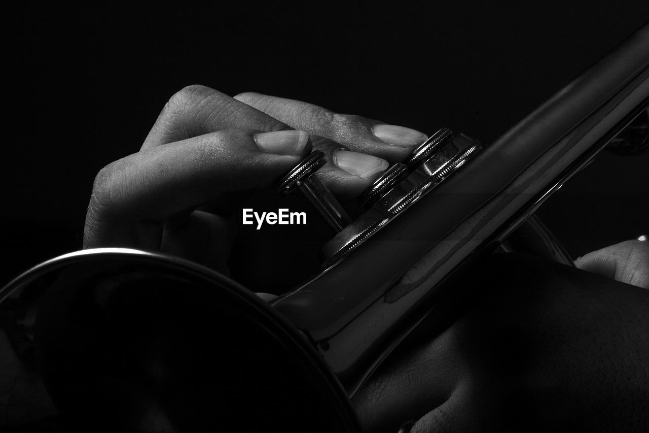 Cropped hand playing trumpet against black background