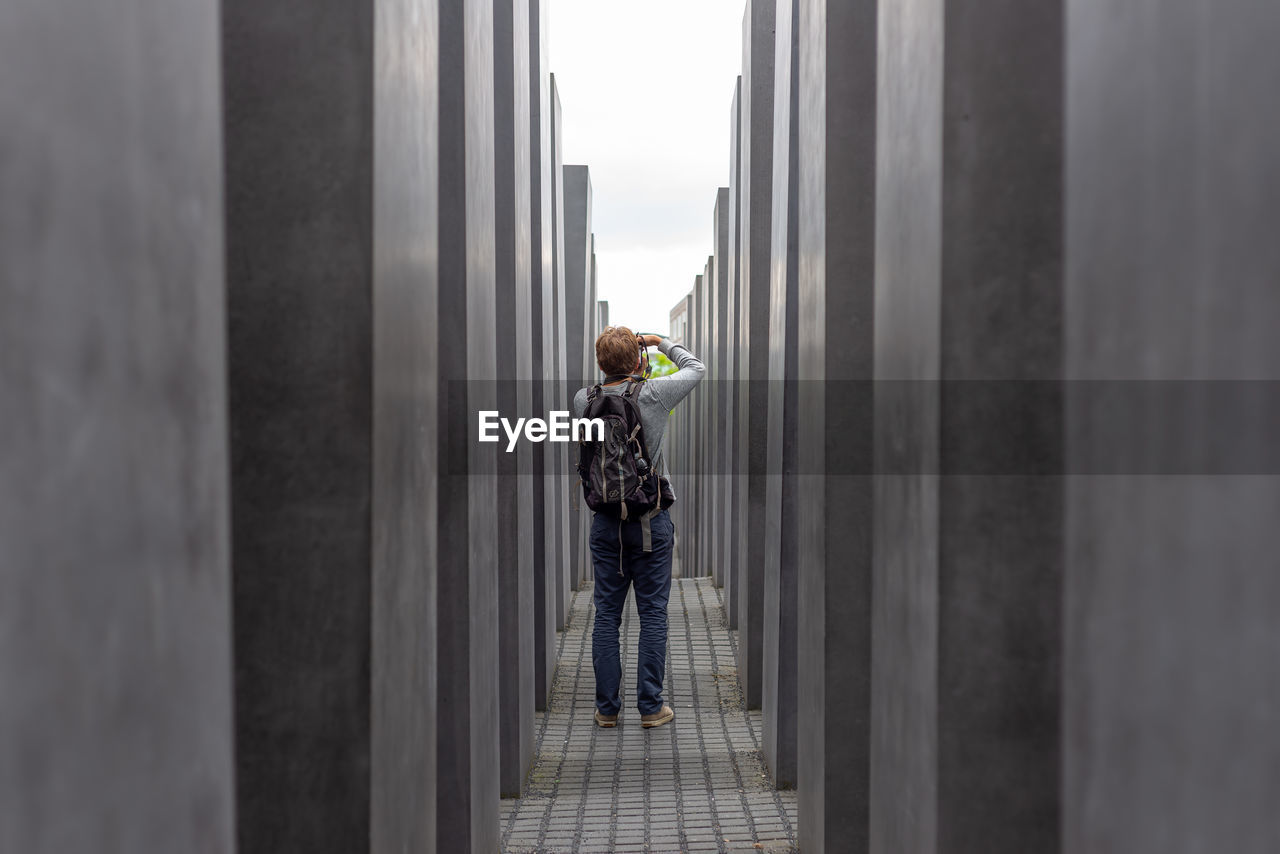 REAR VIEW OF MAN STANDING BY WALL