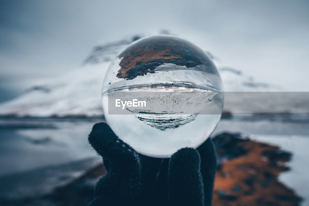 Cropped hand holding crystal ball with reflection by lake