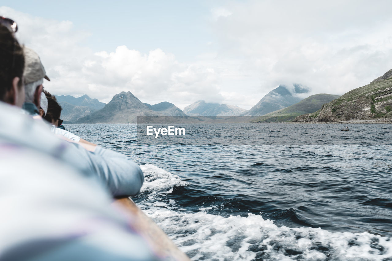 People enjoying on boat amidst scenic sea by mountains against sky