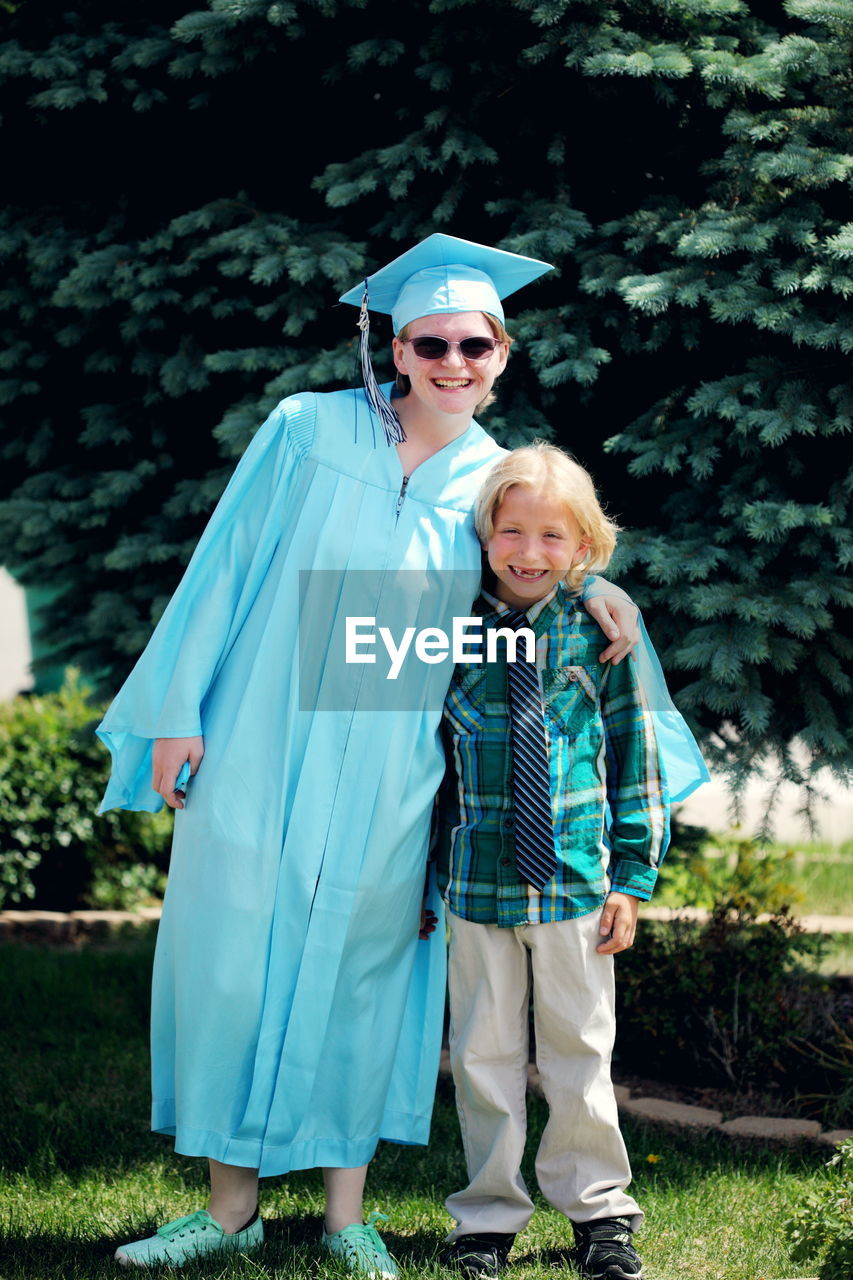 Full length portrait of smiling graduate with brother on field