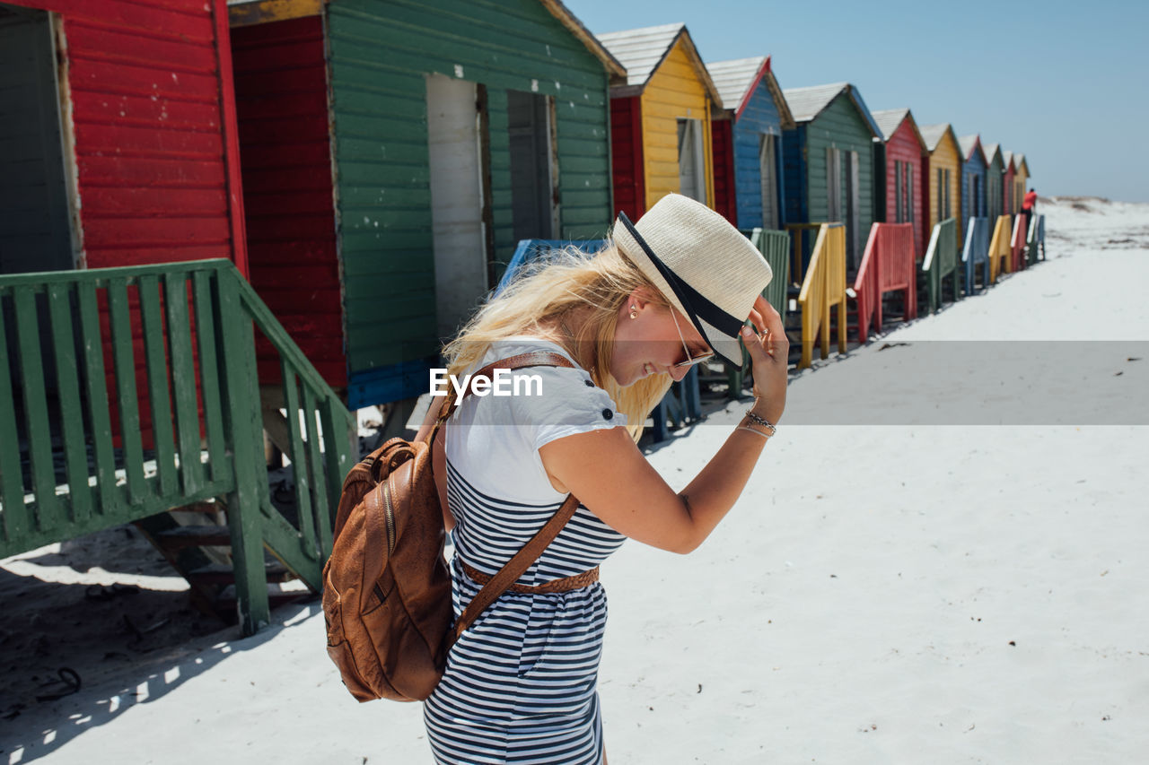 Woman standing at beach against colorful huts and clear blue sky during sunny day