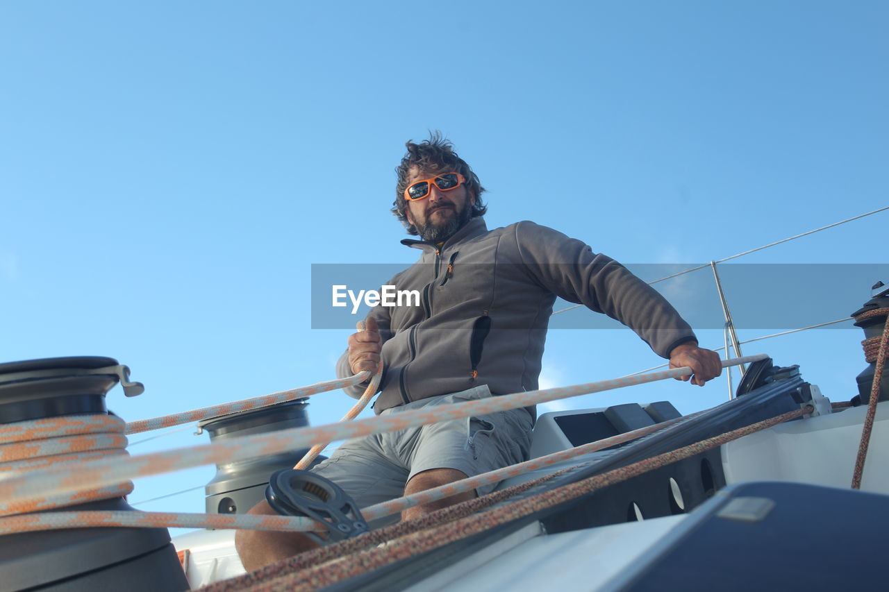 Man pulling rope on sailboat against blue sky