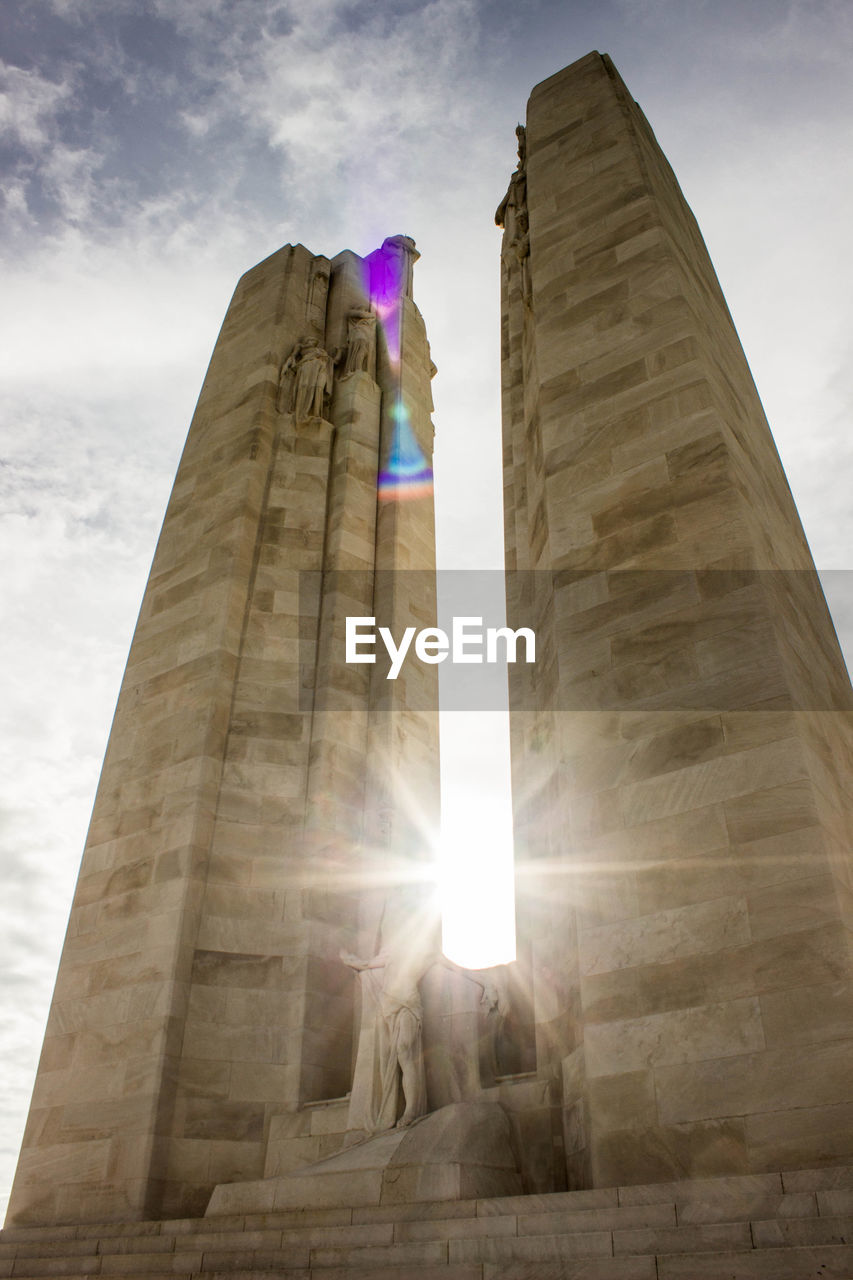 LOW ANGLE VIEW OF SKYSCRAPER AGAINST BRIGHT SUN