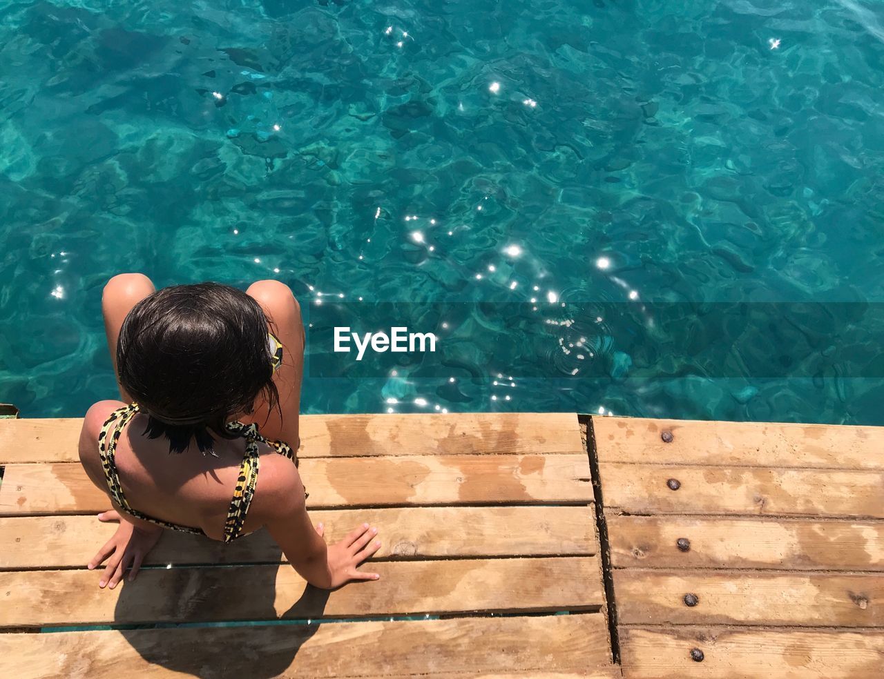 Rear view of girl sitting on pier against the sea