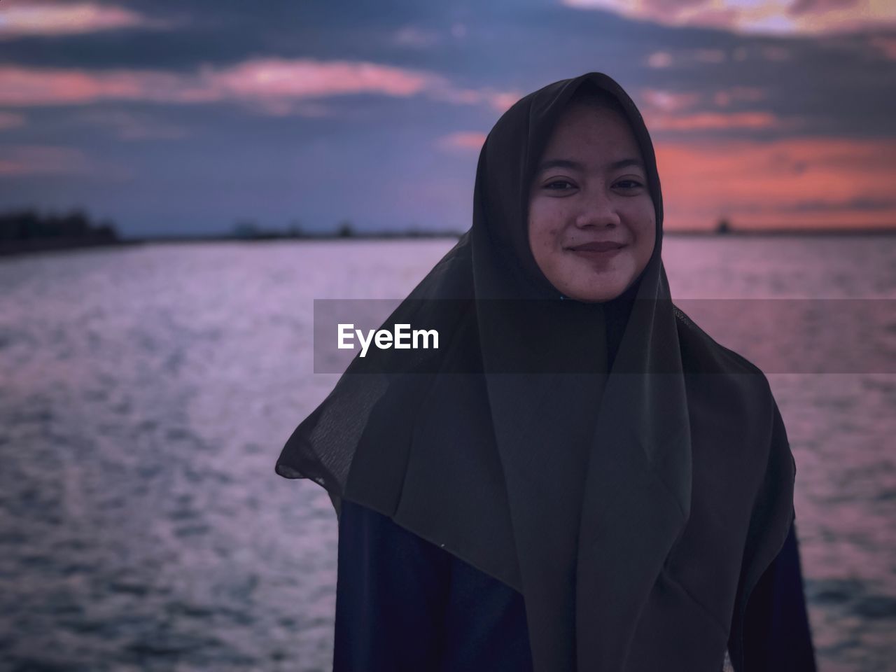 Portrait of smiling woman standing against sea during sunset