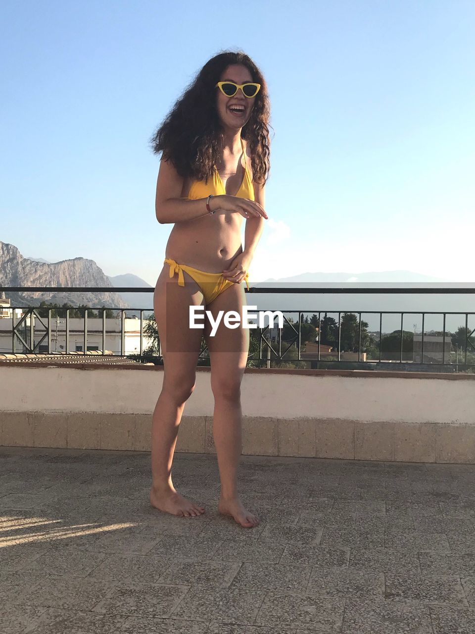 Smiling woman wearing bikini while standing against blue sky