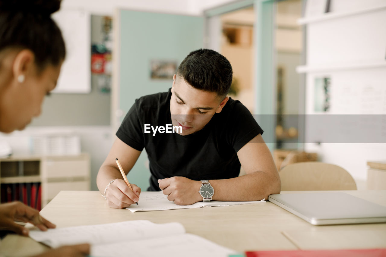 Male teenager writing while sitting in classroom