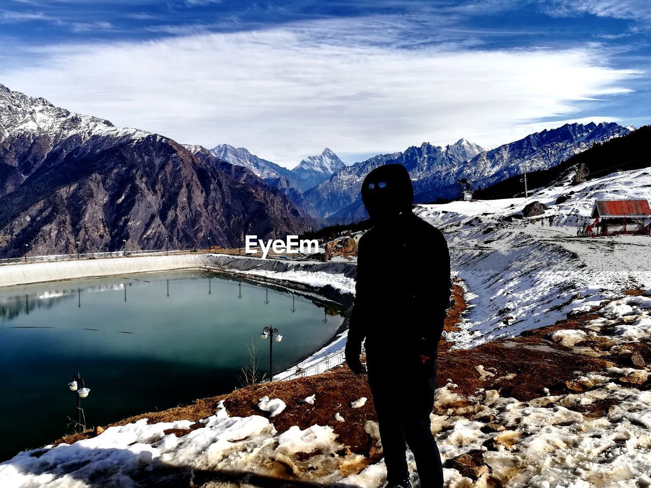 REAR VIEW OF MAN STANDING ON SNOW COVERED MOUNTAIN