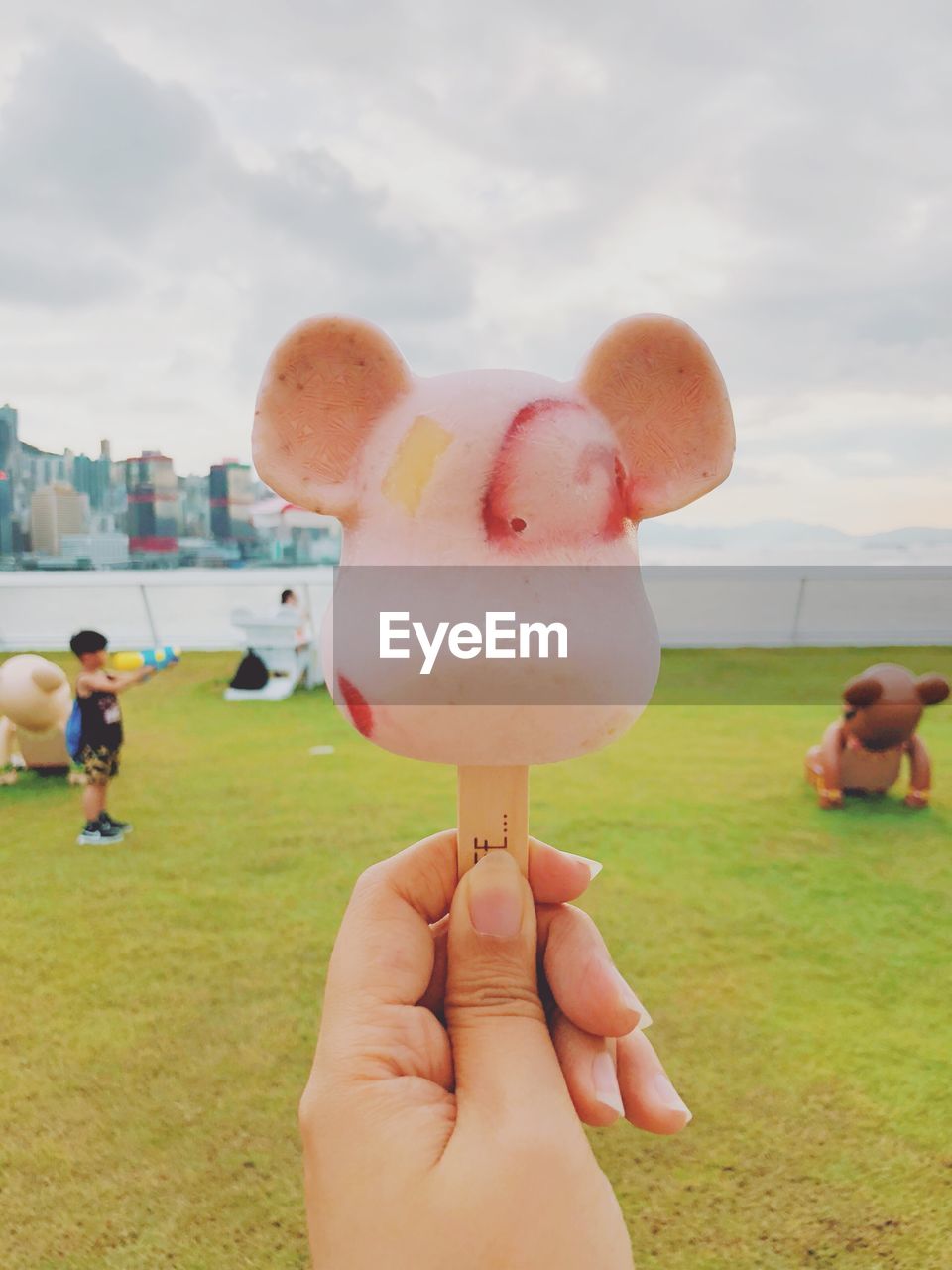 CLOSE-UP OF HAND HOLDING ICE CREAM CONE AGAINST SKY