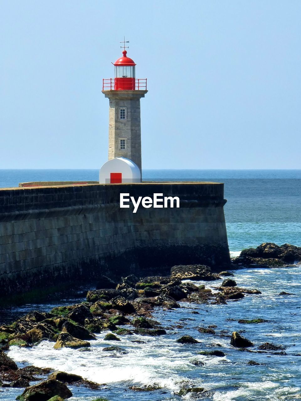 LIGHTHOUSE BY SEA AGAINST BUILDINGS AGAINST SKY