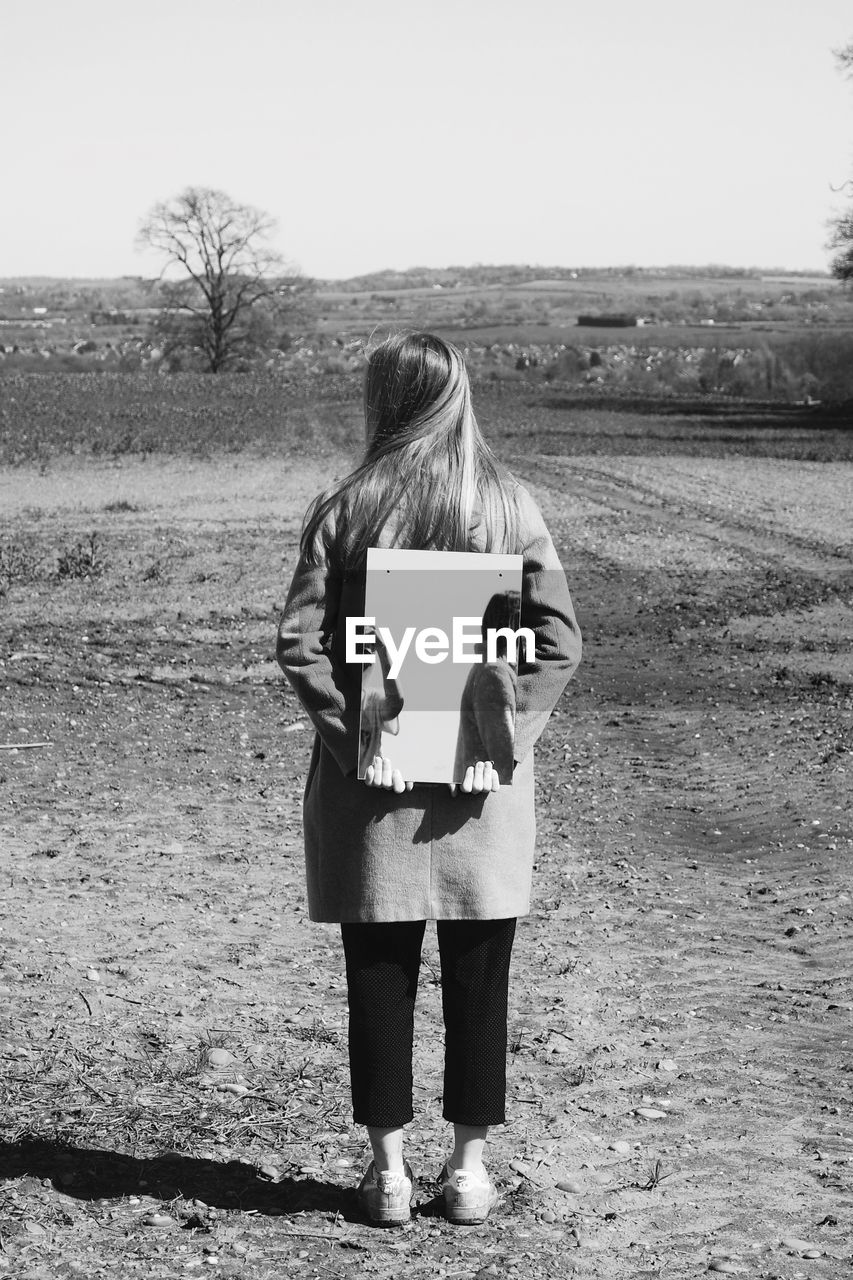 Rear view of woman holding mirror on field