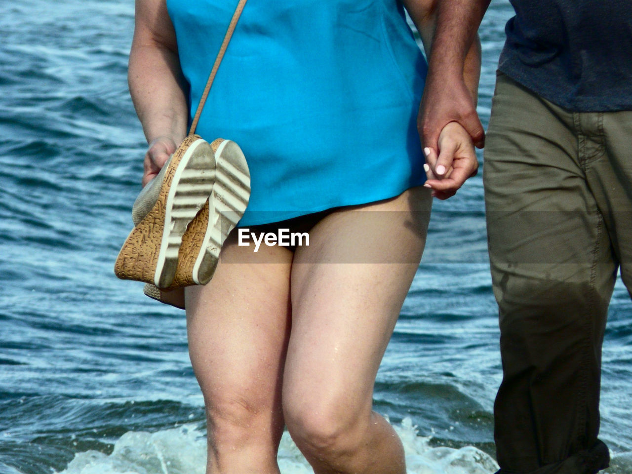 Midsection of couple holding hands while standing against sea