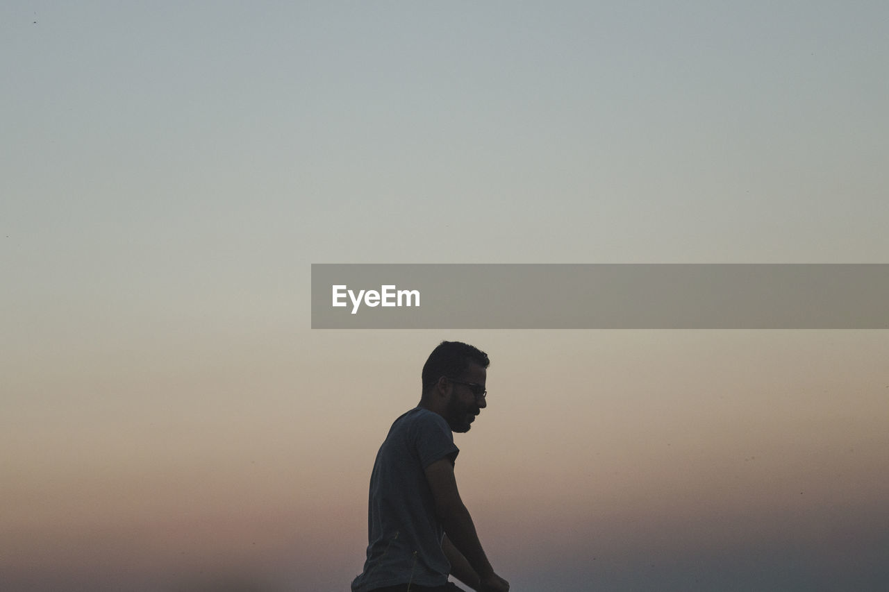 Side view of man standing against clear sky during sunset